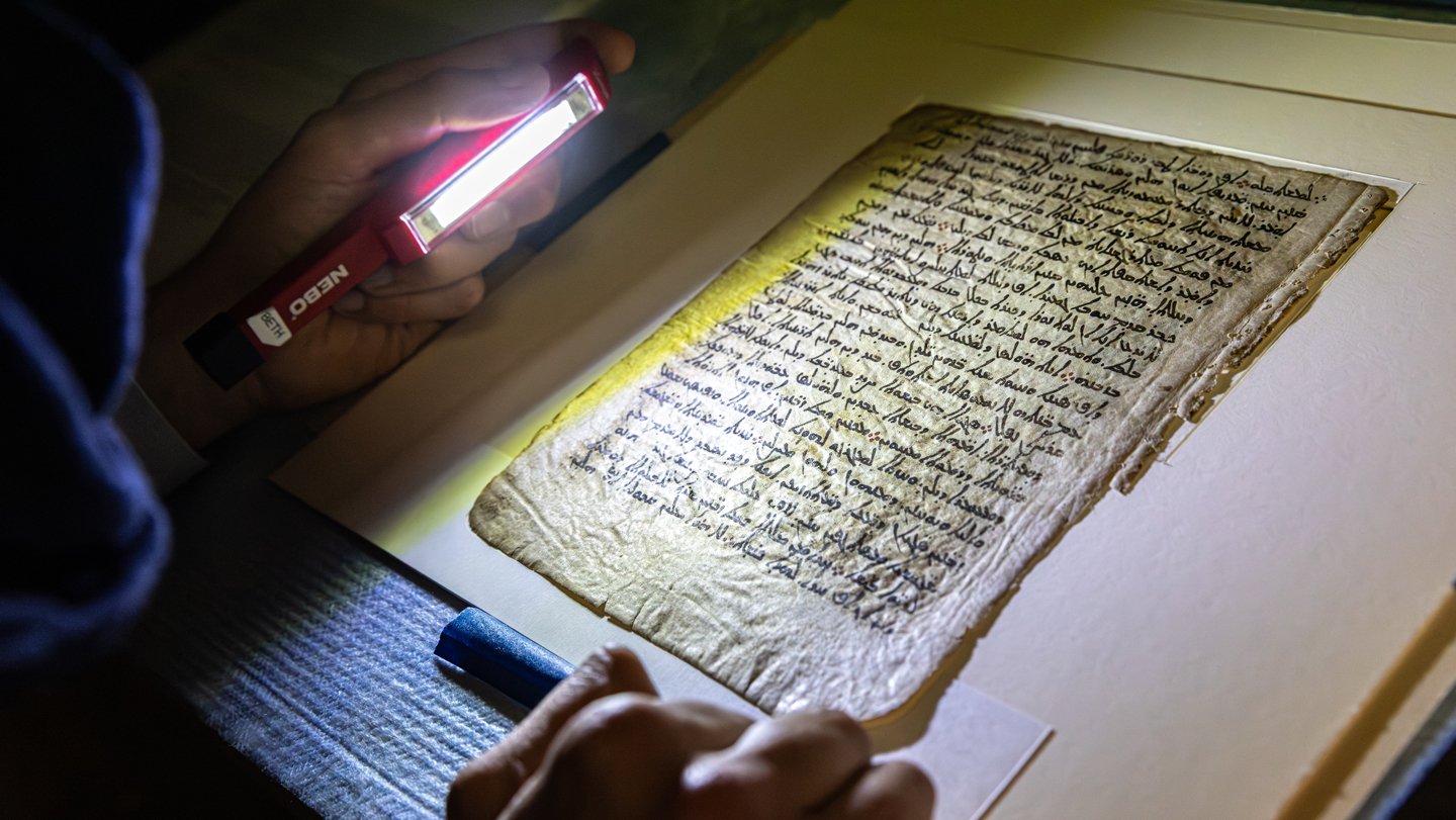 A lamp illuminates Syriac writing on a parchment from the 9th or 10th century A.D., beneath which...
